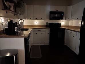 A kitchen with white cabinets, a microwave, a coffee maker, and a trash can.