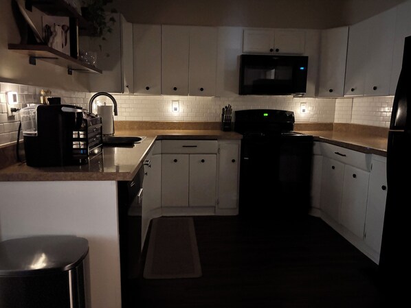 A kitchen with white cabinets, a microwave, a coffee maker, and a trash can.