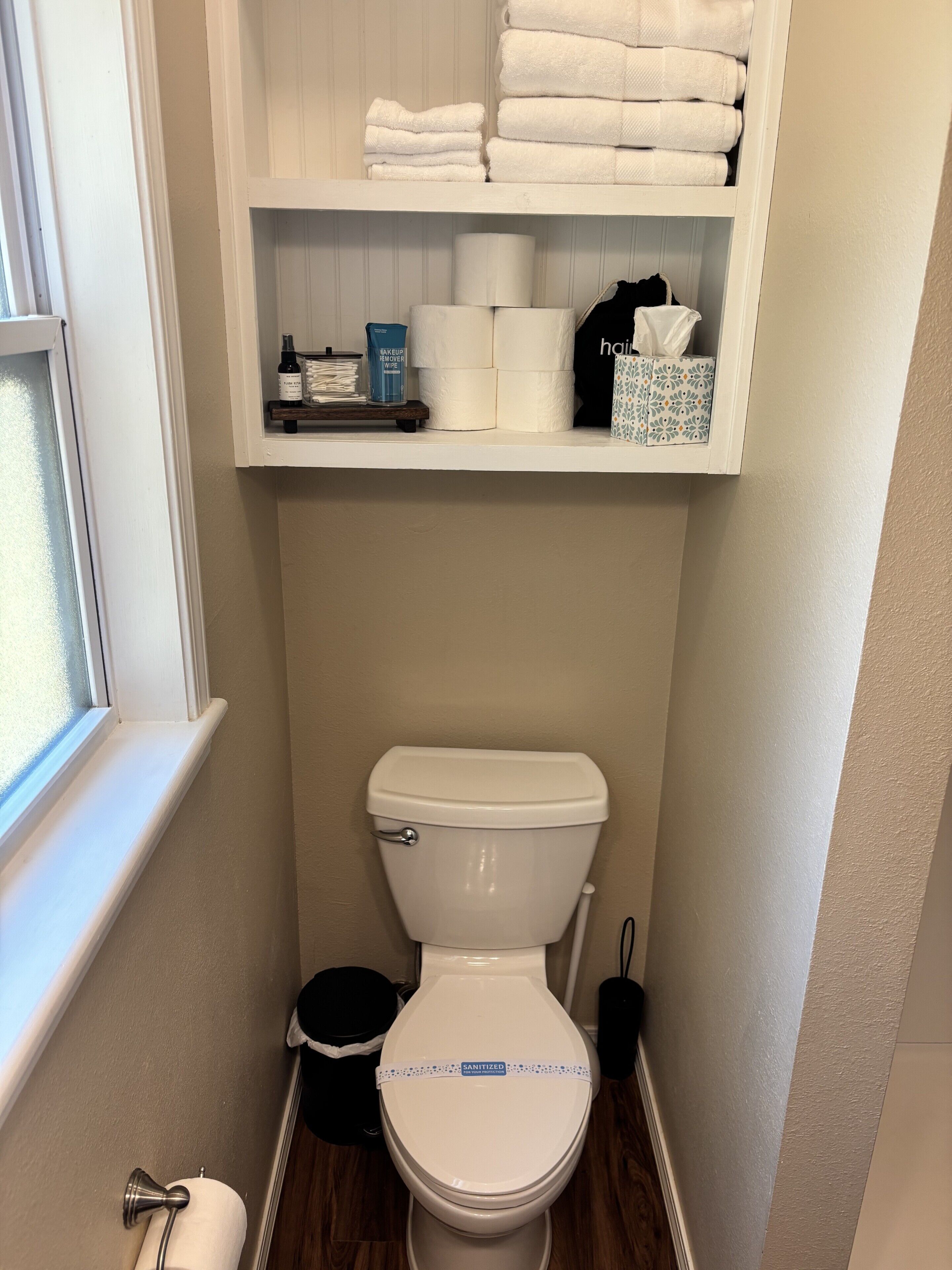 A bathroom with a toilet, a shelf with towels, toilet paper, and a hairbrush.