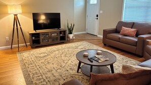 A living room with a television, a sofa, a coffee table, and a floor lamp. - Home Sweet Stillwater 4BR Near OSU (Stillwater)