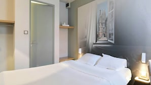 A hotel room with a bed, a nightstand, a wall-mounted lamp, and a door.