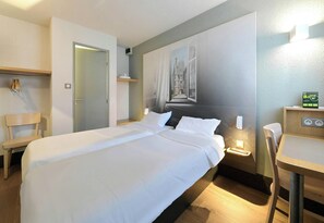Habitación de hotel con una cama grande, un escritorio, una silla, un armario y vistas a un edificio a través de una ventana.