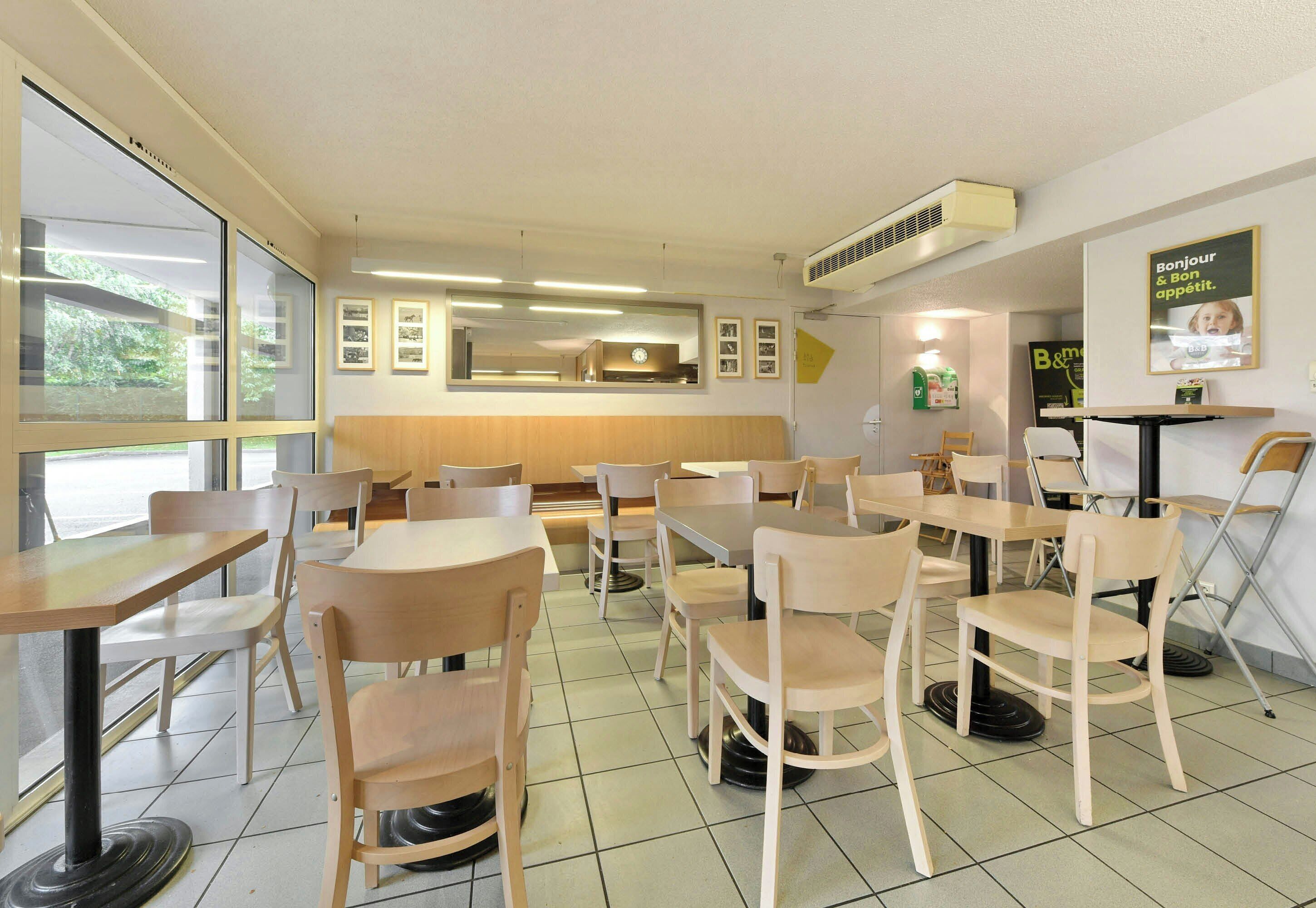 L’intérieur d’un restaurant, avec de nombreuses tables et chaises, une horloge au mur et des tableaux encadrés.
