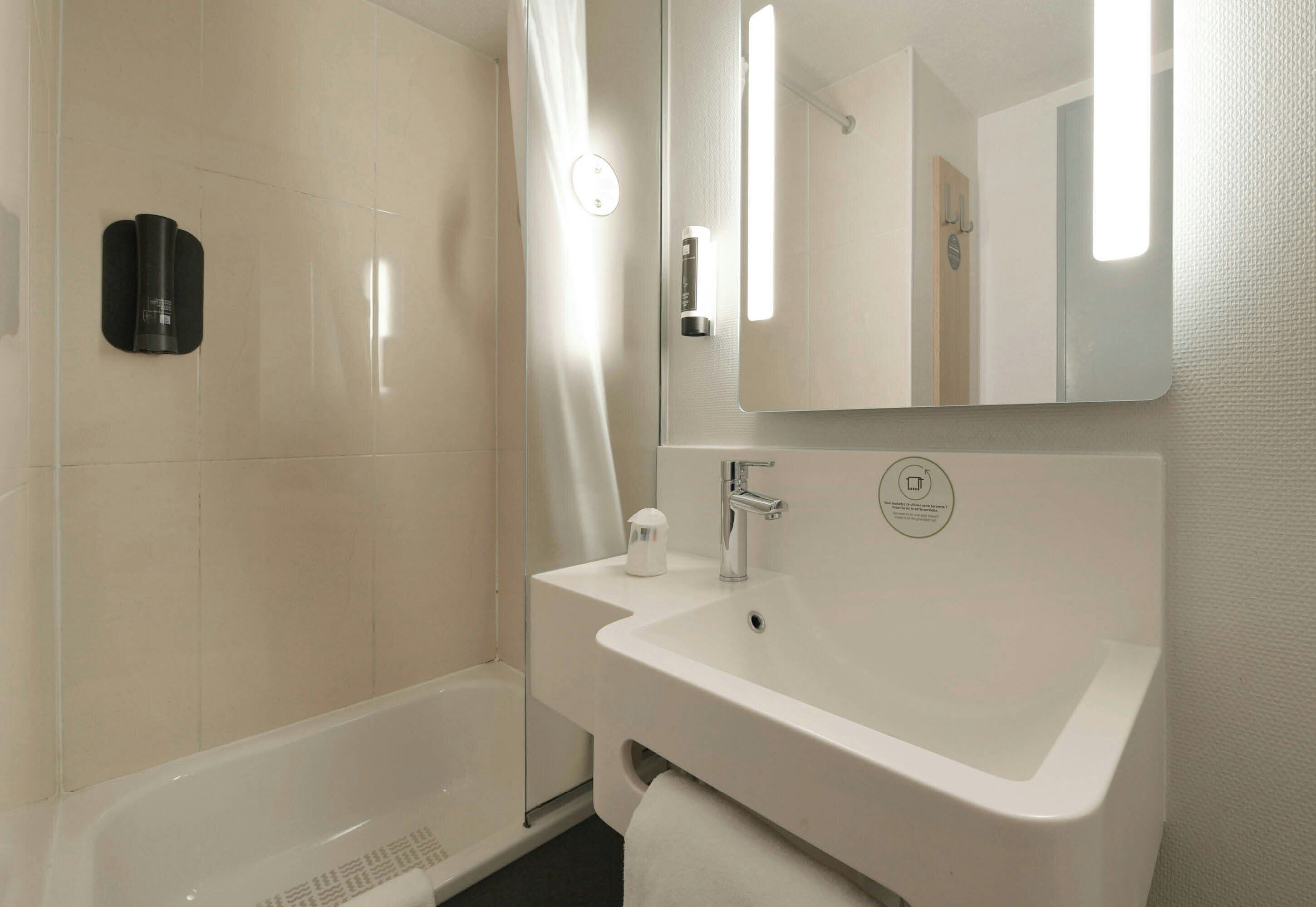 A modern bathroom with a white sink, a mirror, and a shower area.