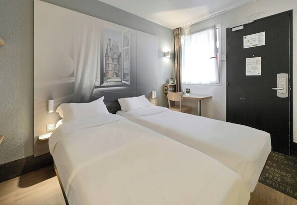 A hotel room with two beds, a window with curtains, a desk, a chair, and a door with a notice on it.