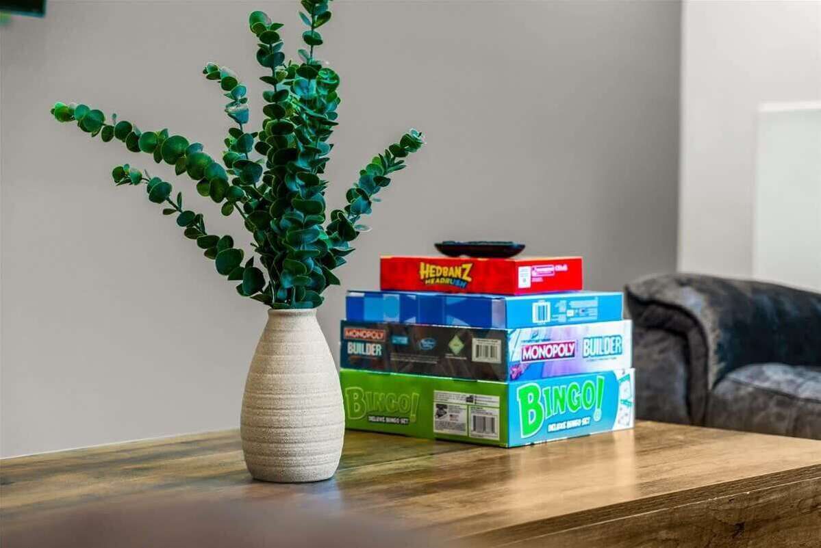 Une plante dans un vase, posée sur une table, avec des boîtes de jeux comme Monopoly et BINGO empilées à côté.