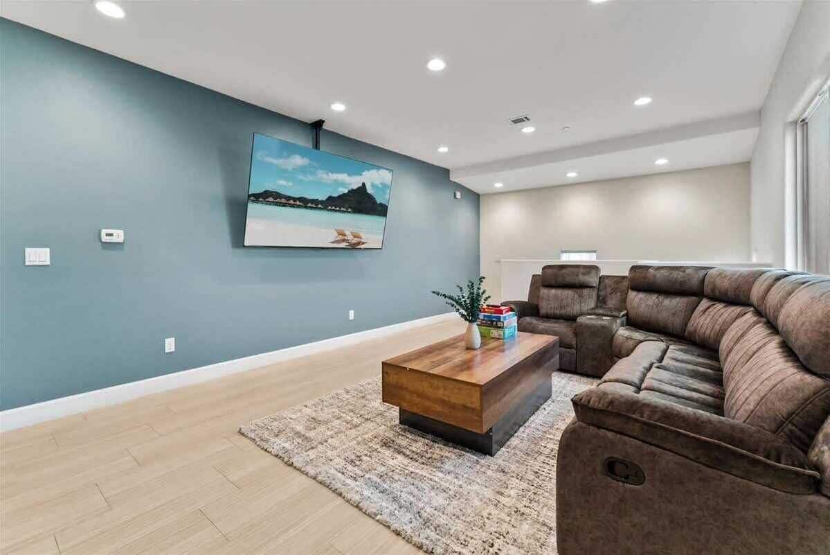 A living room with a sectional sofa, a coffee table, a rug, and a wall-mounted TV.