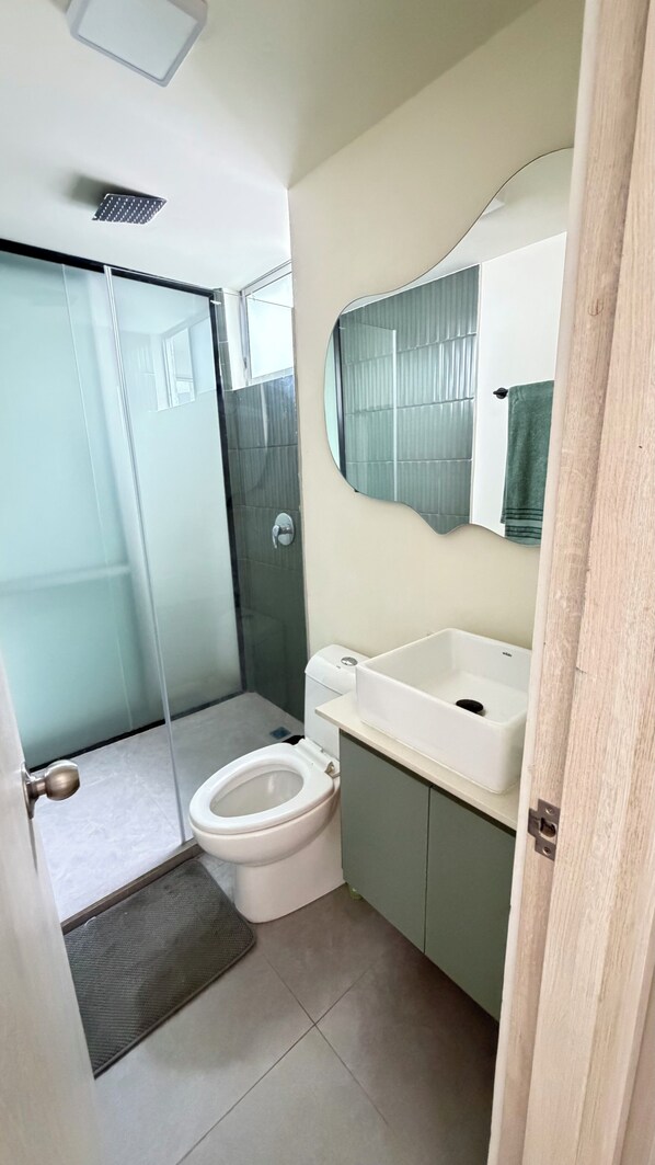 A bathroom with a glass shower enclosure, a toilet, and a sink with a mirror above. - 2-bedroom apartment in charming San Jerónimo with AC and private jacuzzi. (San Jerónimo)