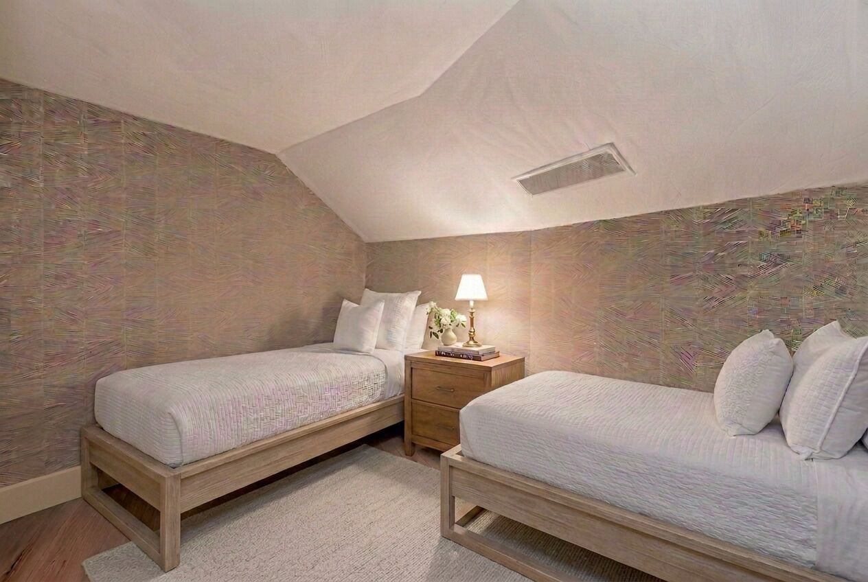 A bedroom with two single beds, a nightstand with a lamp, and a patterned wall.