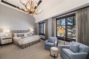 A modern bedroom with a large bed, a chandelier, a sofa, and a view of trees through the window. - Ritz Carlton Bachelor Gulch 2-Bed+Loft Residence (Edwards)