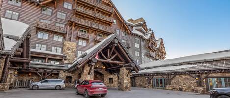 Un immeuble à plusieurs étages, doté d’une façade en pierre, de balcons en bois et d’une entrée aménagée comme un chalet de ski.