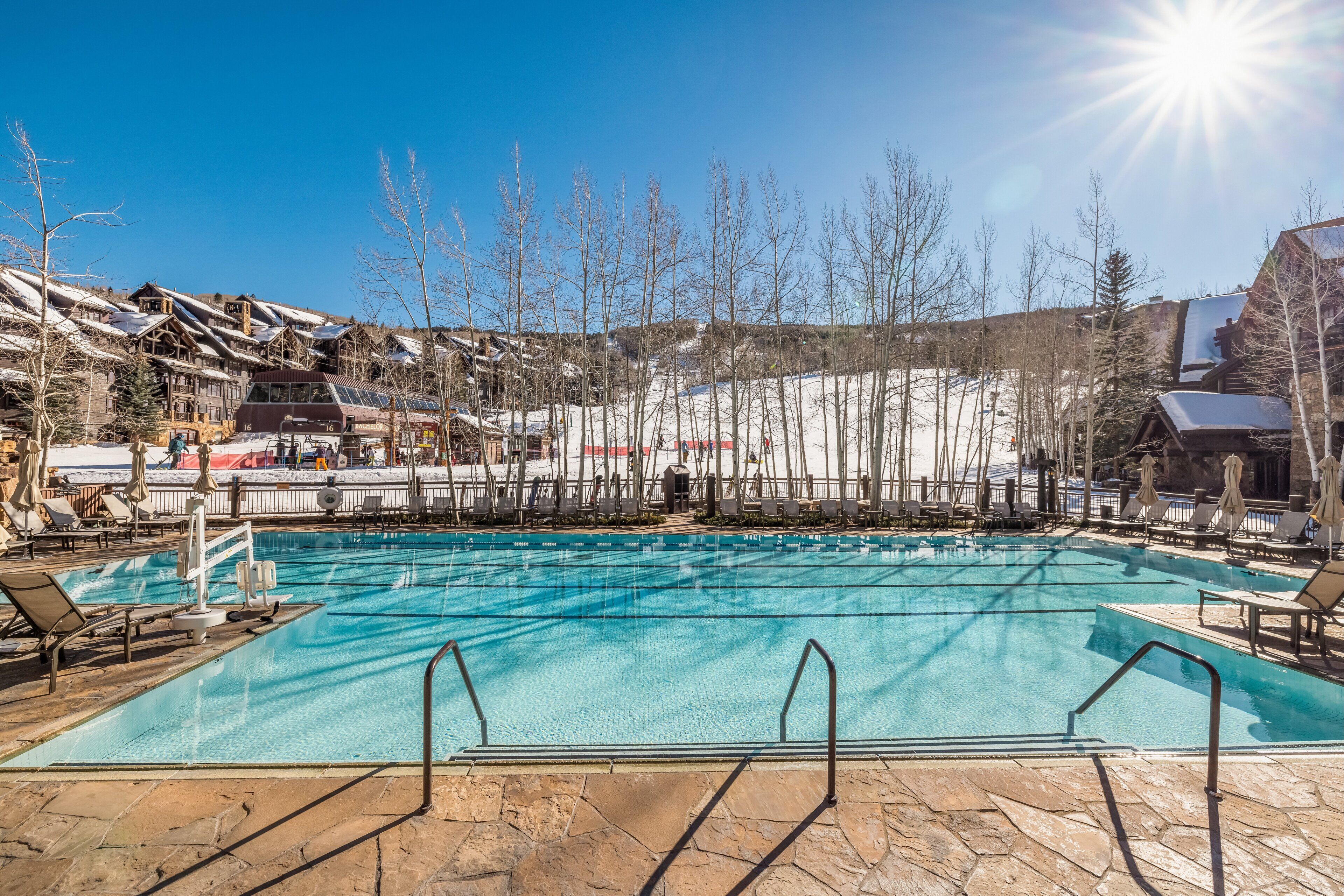 Uma piscina com espreguiçadeiras, rodeada por edifícios e árvores.