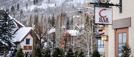 A bar with outdoor seating, a mountain backdrop, and snow-covered trees.