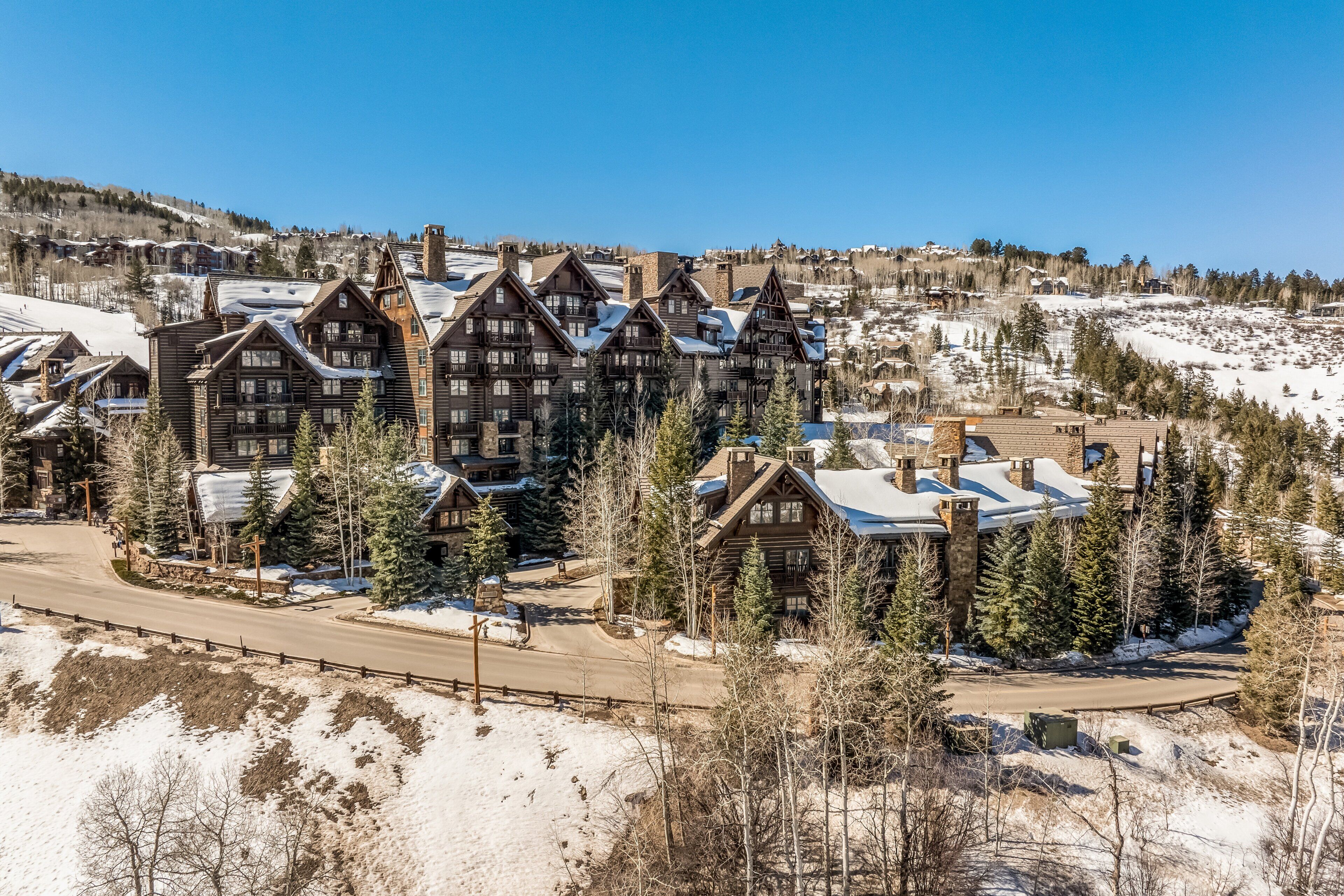 A lodge with multiple wooden buildings, a ski slope in the background, and a clear sky.