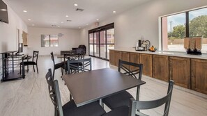 Un comedor moderno con una mesa larga y sillas, una encimera de cocina con equipo para preparar café, y amplios ventanales con vistas al exterior.