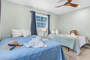 A bedroom with two beds, a ceiling fan, a window with curtains, and a sign on the wall. - Canal Retreat with Heated Pool, Beach Walk & Putting Green Escape - Mar el Agua - Roelens (Fort Myers Beach)
