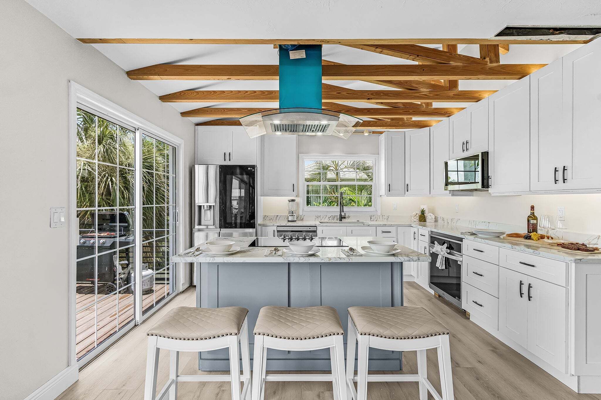 Een moderne keuken met een centraal eiland, witte kasten en een houten plafond.