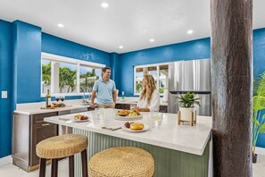 A modern kitchen with blue walls, a central island, and a large window. - Canal Retreat with Heated Pool, Beach Walk & Putting Green Escape - Mar el Agua - Roelens (Fort Myers Beach)