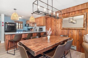 A modern kitchen with wooden accents, a dining area with a large wooden table, and a built-in island with bar stools. - Howling Wolf Winter Park Ski/Hike/Bike Condo (Winter Park)