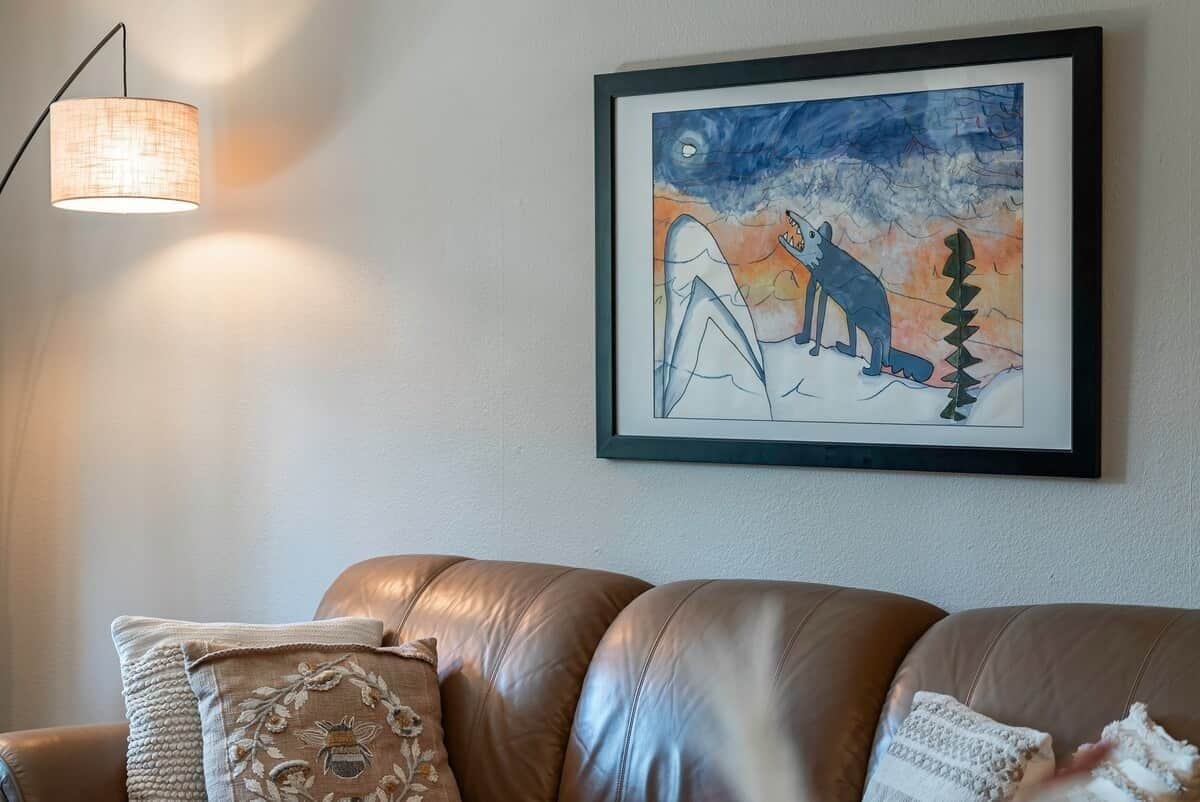 A framed artwork depicting a wolf and a dog on a snowy landscape, a brown leather sofa, and a wall-mounted lamp.