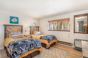 A bedroom with two beds, a window with a view of trees, and a mirror on the wall. - Howling Wolf Winter Park Ski/Hike/Bike Condo (Winter Park)