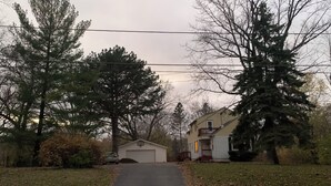 Ein Weg führt zu einem Haus mit Garage, umgeben von Bäumen und einer Rasenfläche.