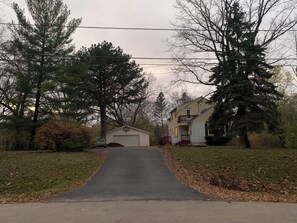 A residential driveway leading to a house with a garage, surrounded by trees and a grassy area. - Cozy 2 bedroom Upper Duplex w/ Bonus Room (New Berlin)