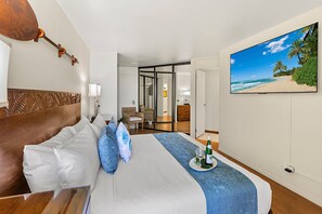 Ein Hotelzimmer mit Bett, Blick auf einen Strand durch eine Glastür und einem Gemälde einer Strandlandschaft.