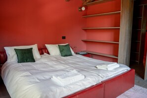 A bed with white bedding and green pillows in a room with red walls and a wooden headboard.