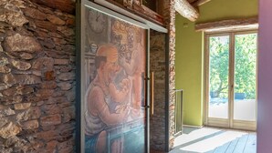 A room with a stone wall, a large glass door with a mural, and a view of greenery outside.