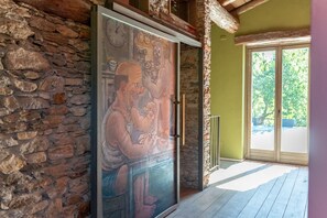 A room with a stone wall, a large glass door with a mural, and a view of greenery outside.