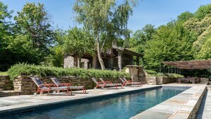 A swimming pool with lounge chairs, a stone building, and lush greenery in the background.