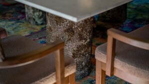 A table with a textured stone base, surrounded by wooden chairs with cushioned seats.