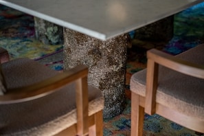 A table with a textured stone base, surrounded by wooden chairs with cushioned seats.
