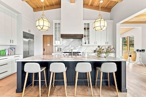 Una cocina moderna con una isla grande, taburetes de bar e iluminación colgante.