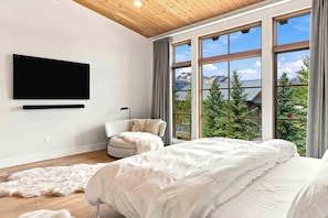 Un dormitorio con una cama grande, televisión montada en la pared y vistas a las montañas a través de amplios ventanales.