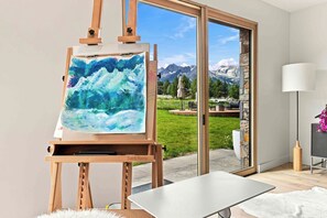 A room with a large painting on an easel, a view of mountains through a glass door, and a modern interior design.