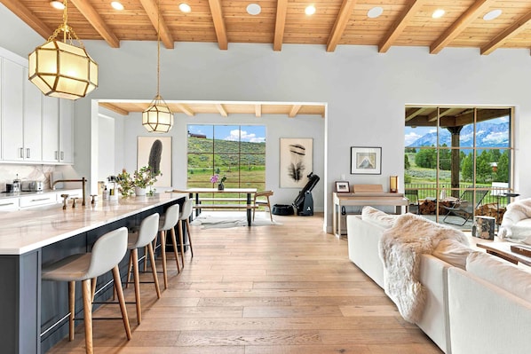 A spacious kitchen with a central island, bar stools, and a view of a mountainous landscape through large windows.
