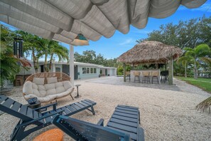 An outdoor seating area with lounge chairs, a thatched-roof structure, and a building with a light blue facade. - Unique 4-bedroom house with pool and gulf access in lovely Fort Myers (Fort Myers)