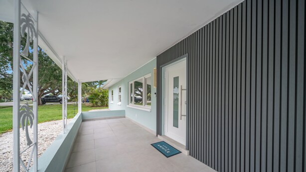Une allée couverte mène à un bâtiment au design moderne, doté d’un sol de couleur claire et d’une porte ornée de motifs à rayures verticales.