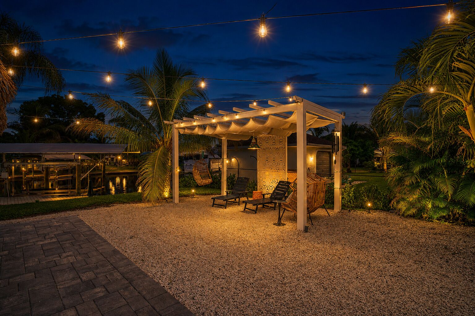 Un espace extérieur aménagé avec un coin salon, une pergola, des guirlandes lumineuses et des palmiers.