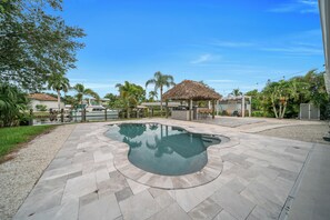 A swimming pool with a curved design, surrounded by a patio area with stone tiles. - Unique 4-bedroom house with pool and gulf access in lovely Fort Myers (Fort Myers)