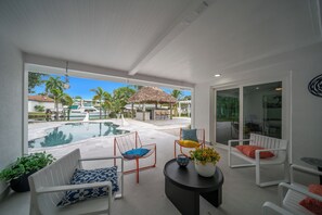 Ett modernt utomhusområde med sittplatser, en pool, solstolar och en byggnad med halmtak.