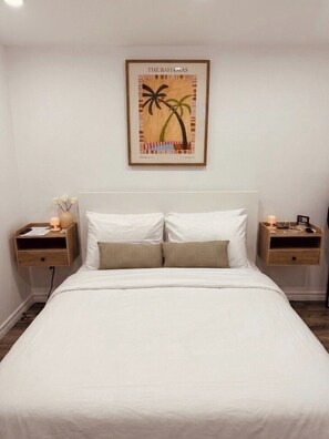 A bedroom with a bed, two nightstands, a framed picture of palm trees, and a night lamp on each side. - Cozy Detached Garden Guesthouse | Private Studio (Hamilton)