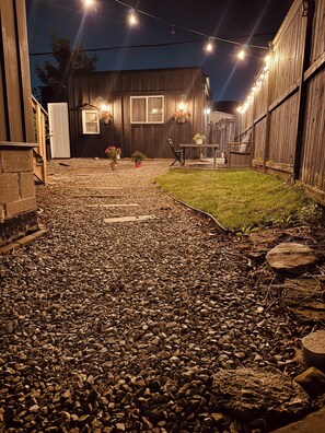 A backyard with a gravel path leading to a wooden house, string lights, and potted plants. - Cozy Detached Garden Guesthouse | Private Studio (Hamilton)