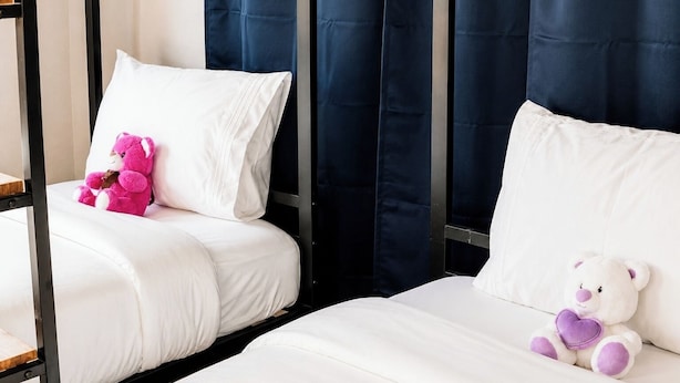 Een hotelkamer met twee bedden, waarvan er een een roze knuffel heeft en de ander een witte.