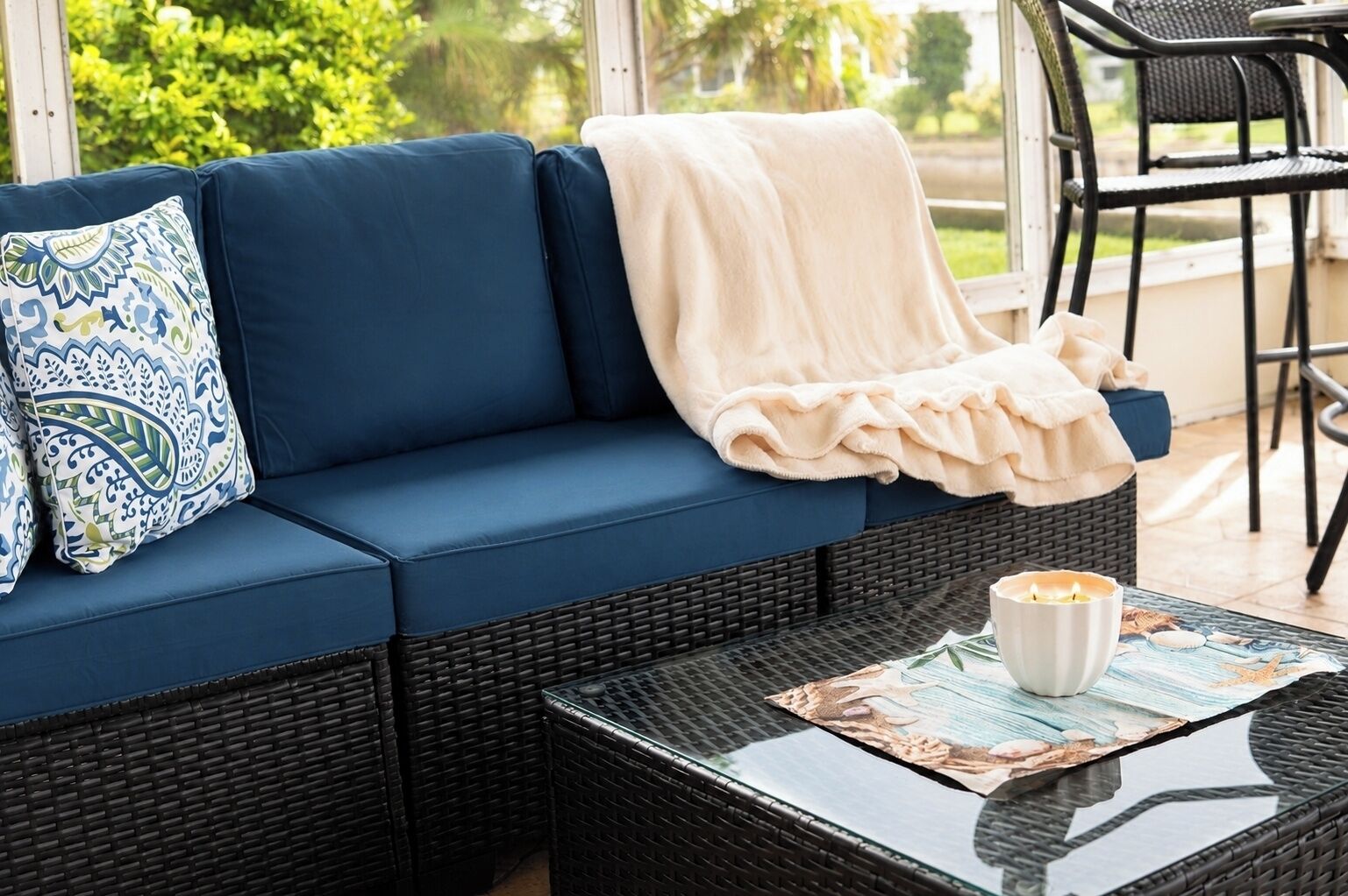 A blue sofa with a patterned pillow, a white throw blanket, and a candle on a glass table.