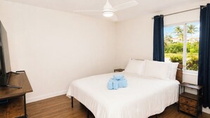 Habitación de hotel con cama, escritorio, ventilador de techo y ventana con cortinas.