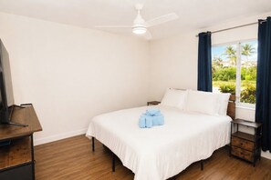 A hotel room with a bed, a desk, a ceiling fan, and a window with curtains.