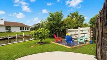 A backyard with a small pond, a wooden fence, and colorful Adirondack chairs.